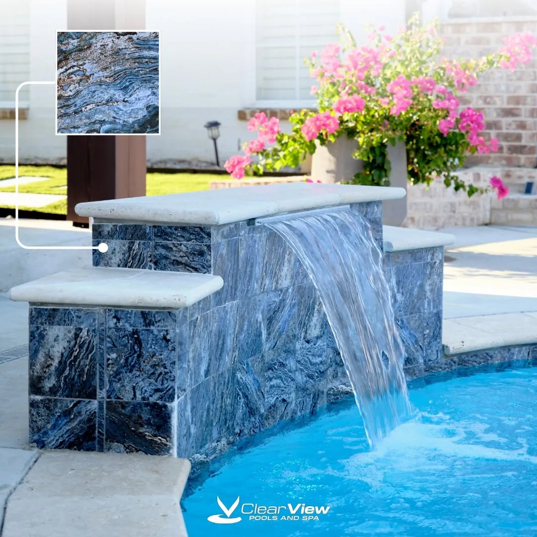 Blue tile spillway pouring water into a backyard pool