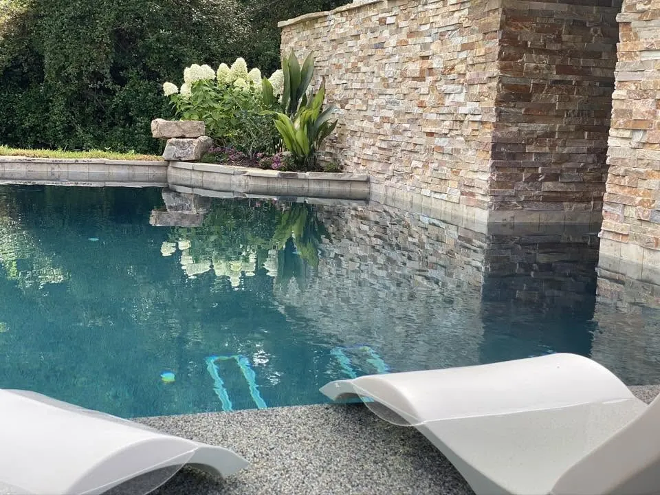 Clear pool beside a stacked stone wall with white loungers