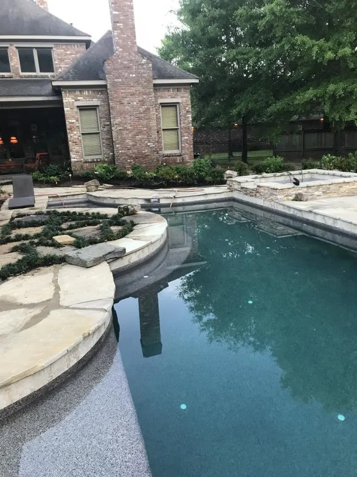 Pool with steps and natural stone surround beside a brick house